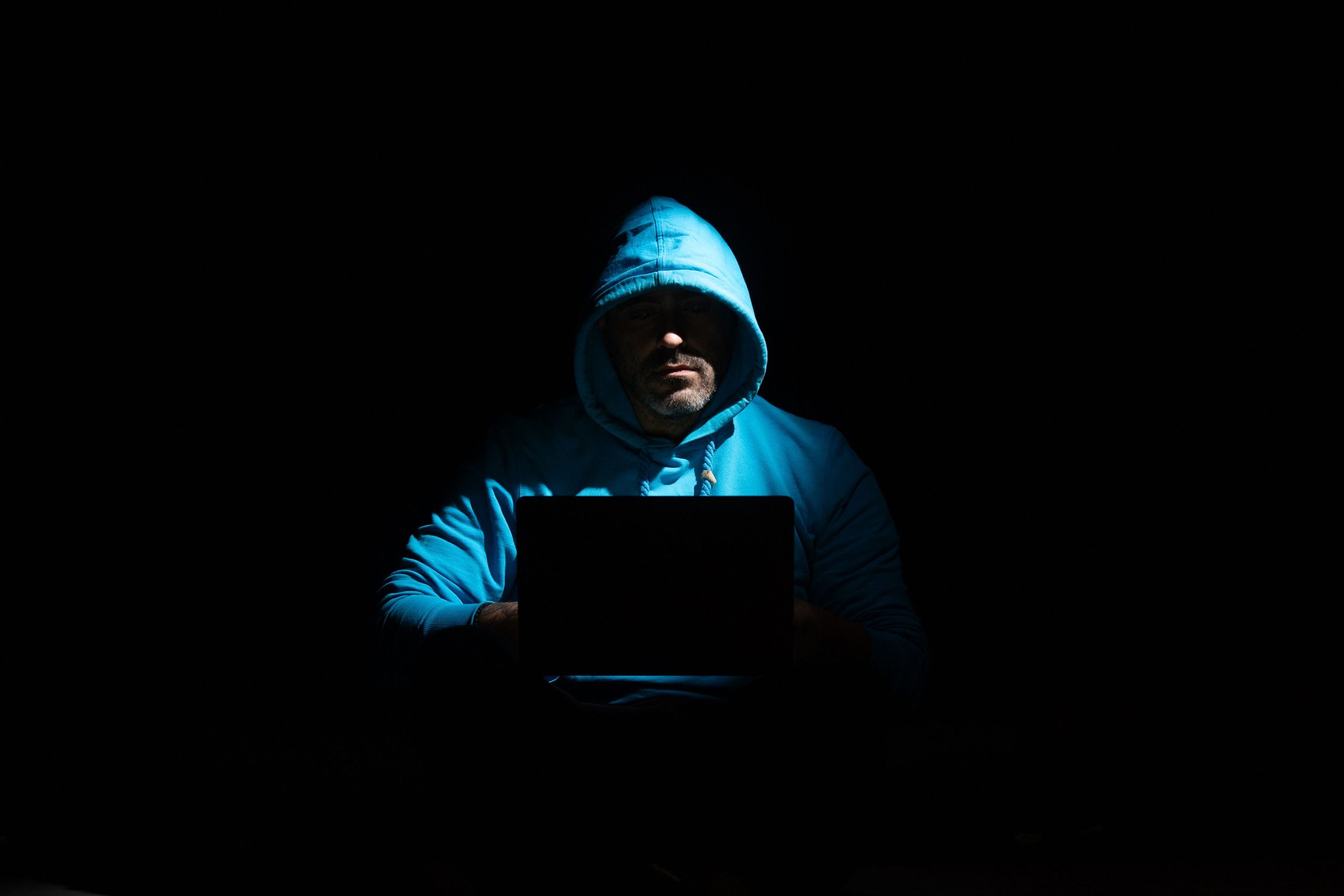 Personne en hoodie utilisant laptop dans l'obscurité mystérieuse