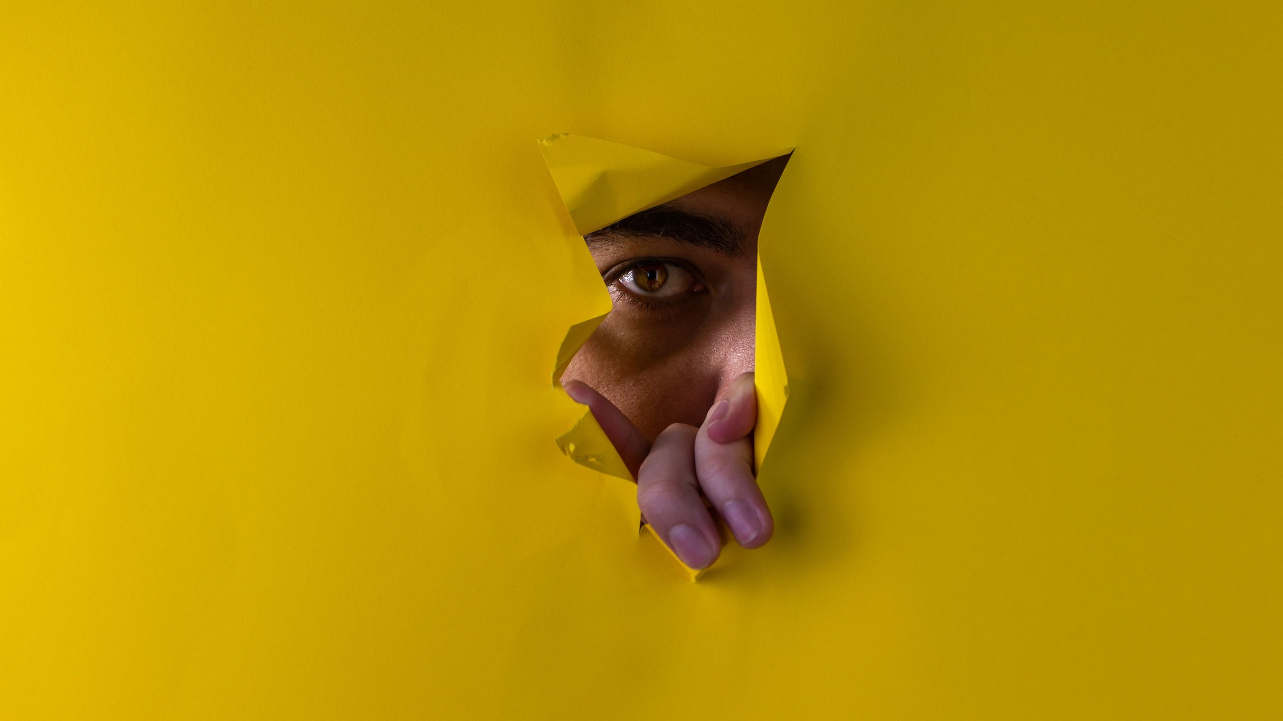 Œil curieux épiant à travers du papier jaune déchiré