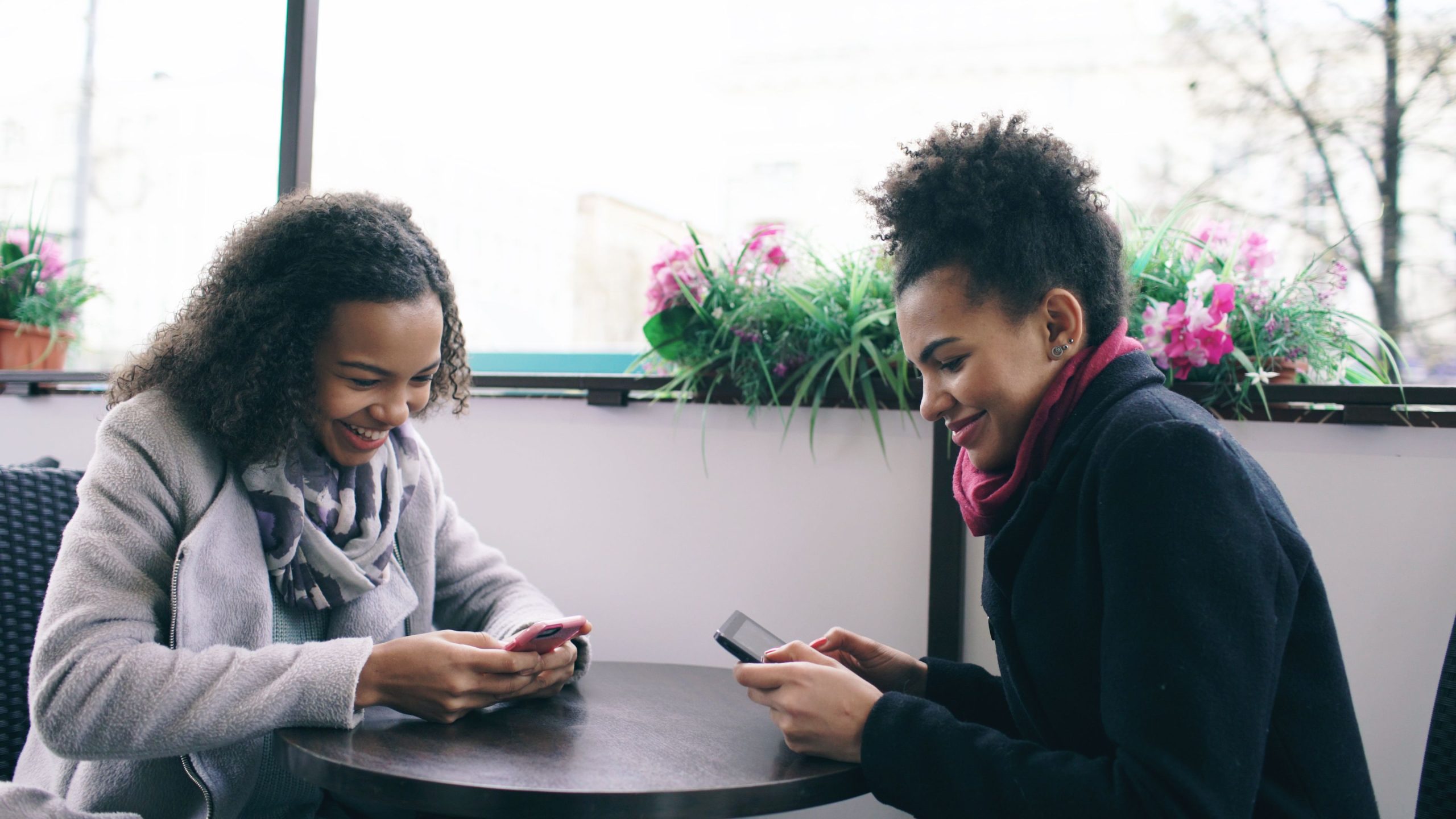 Deux amies rient en prenant un café avec leurs téléphones